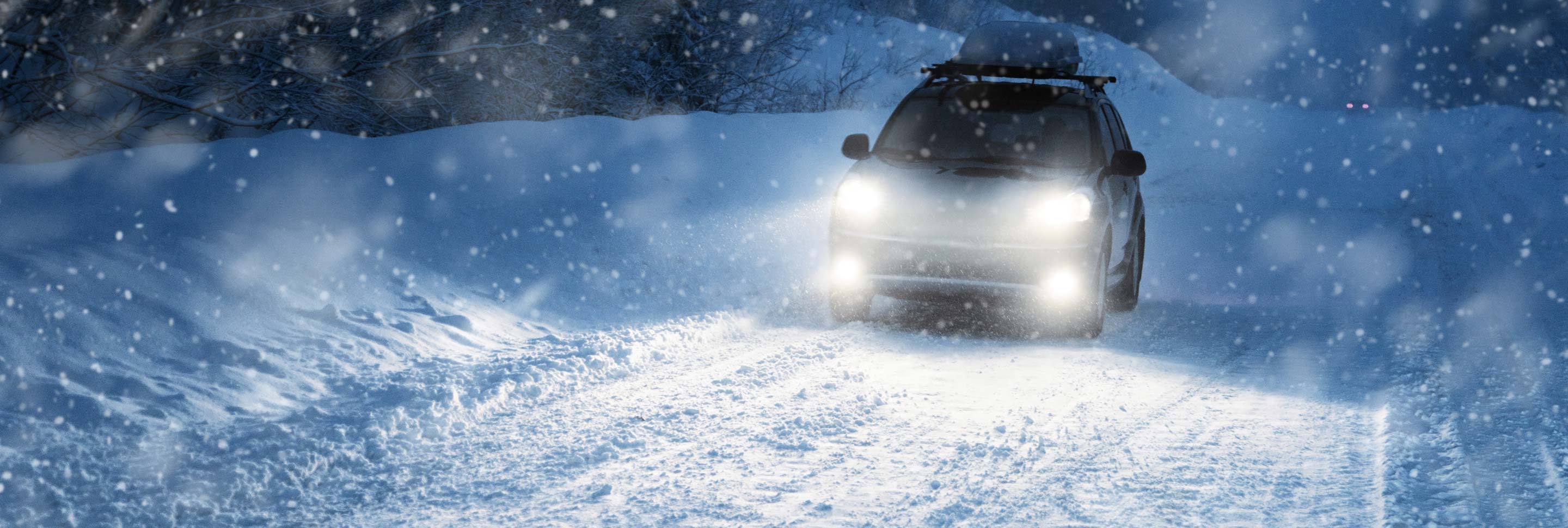 A car driving on a snowy highway at night.
