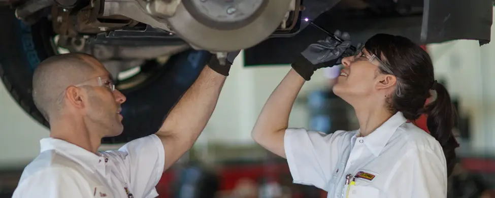 A pair of Les Schwab employees checking a vehicle's breaks while it sits on a post lift