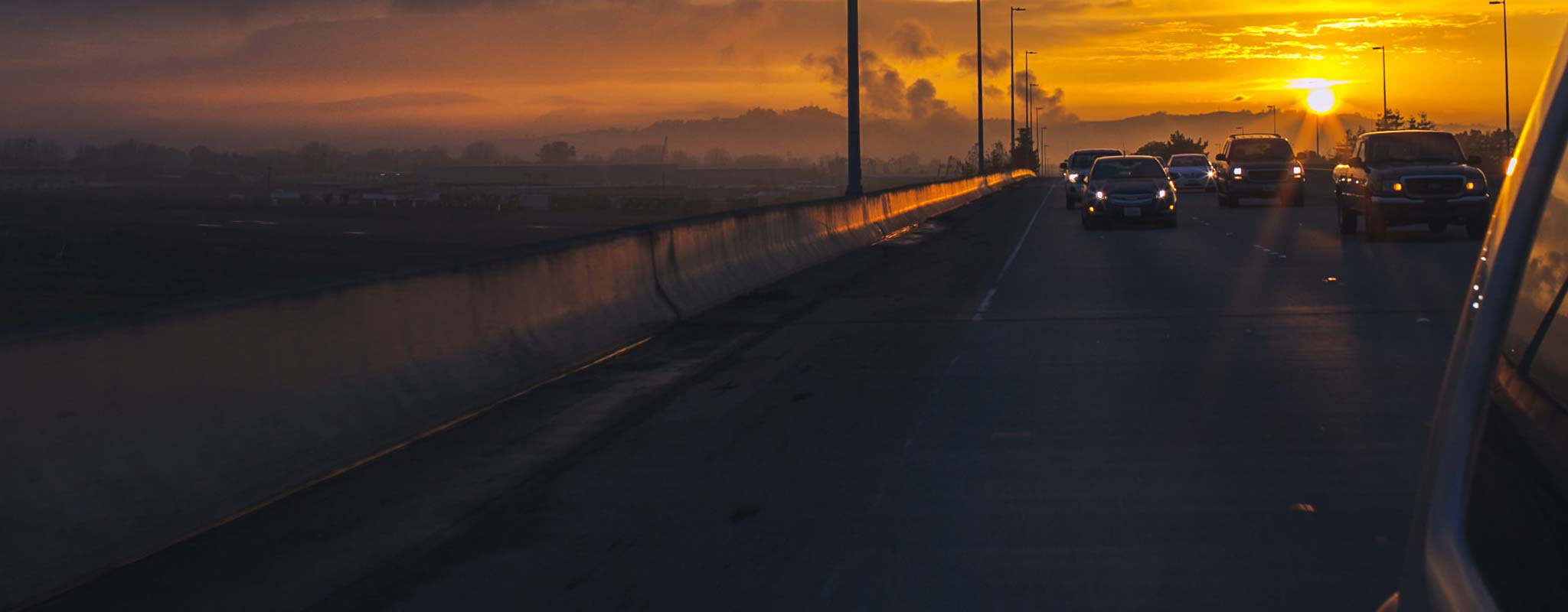 Cars running headlights as the sun sets behind them.