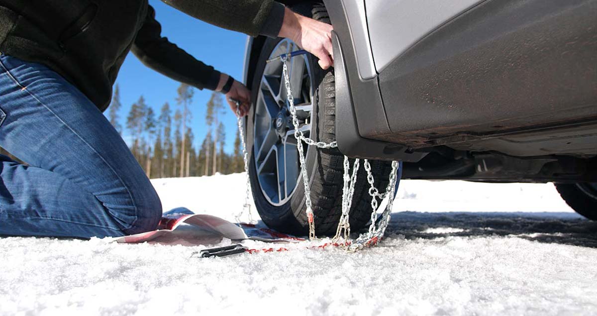 Man pulling tire chain up around tire.