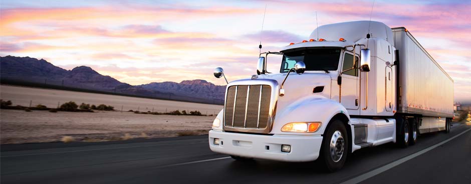 White semi-truck driving down the highway during sunset.