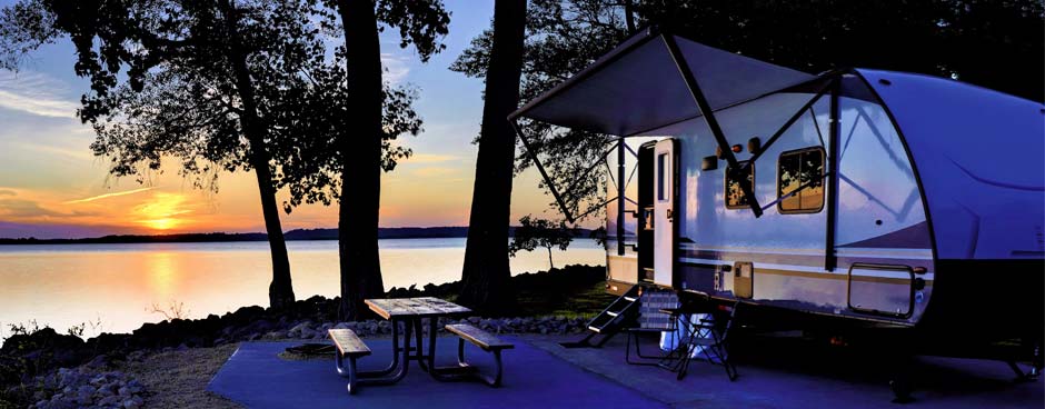 Travel trailer next to a lake at sunset.