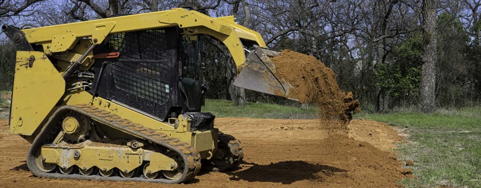 Skid steer moving dirt in it's loader