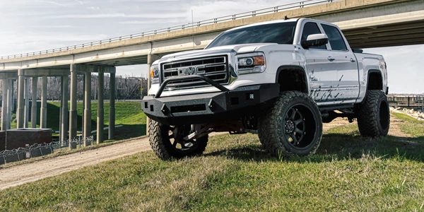 A lifted pickup truck sits atop a hill framed by a nearby roadway