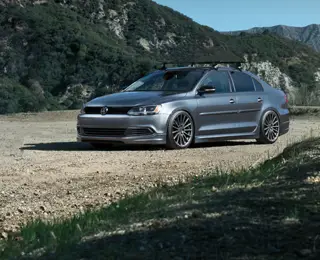 A platinum gray Volkswagen seden with a rooftop bike rack parked on a dirt road out in the country.