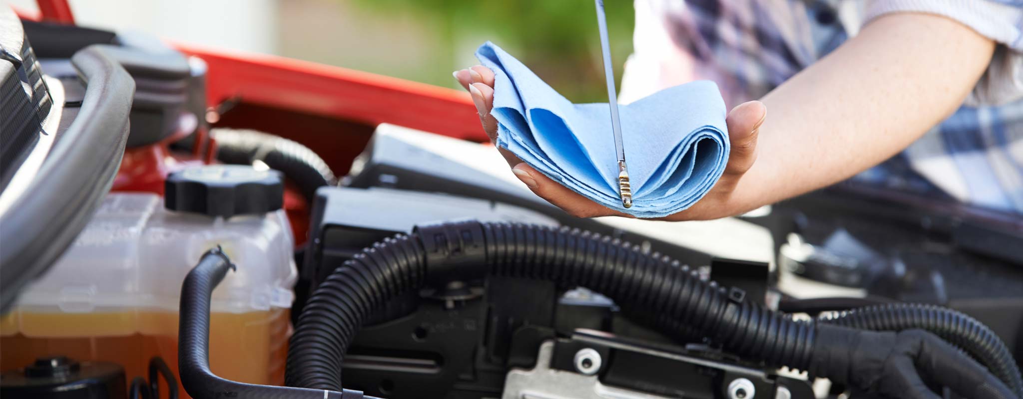 A close-up of a woman checking the oil on her car.