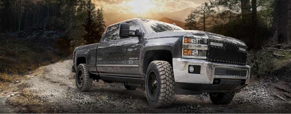 A black pickup truck driving on a dirt road at dusk