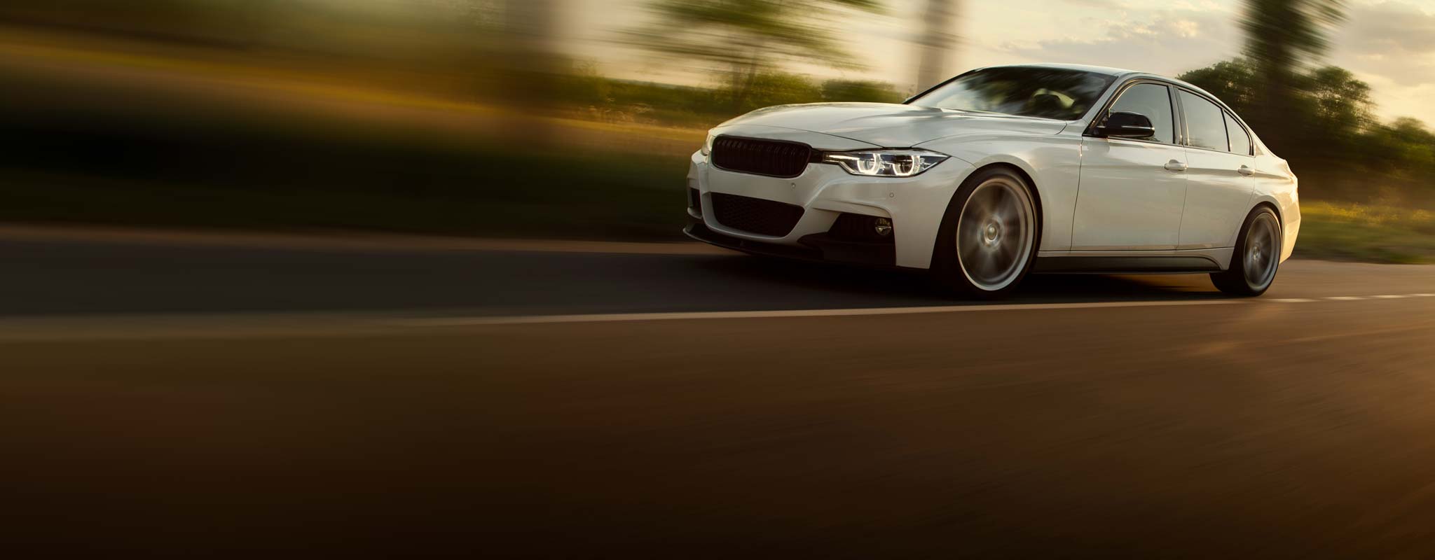 White BMW style car speeding down road.