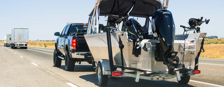 Black pickup pulling an aluminum boat on freeway.