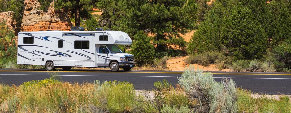 RV parked in front of orange rock cliff.